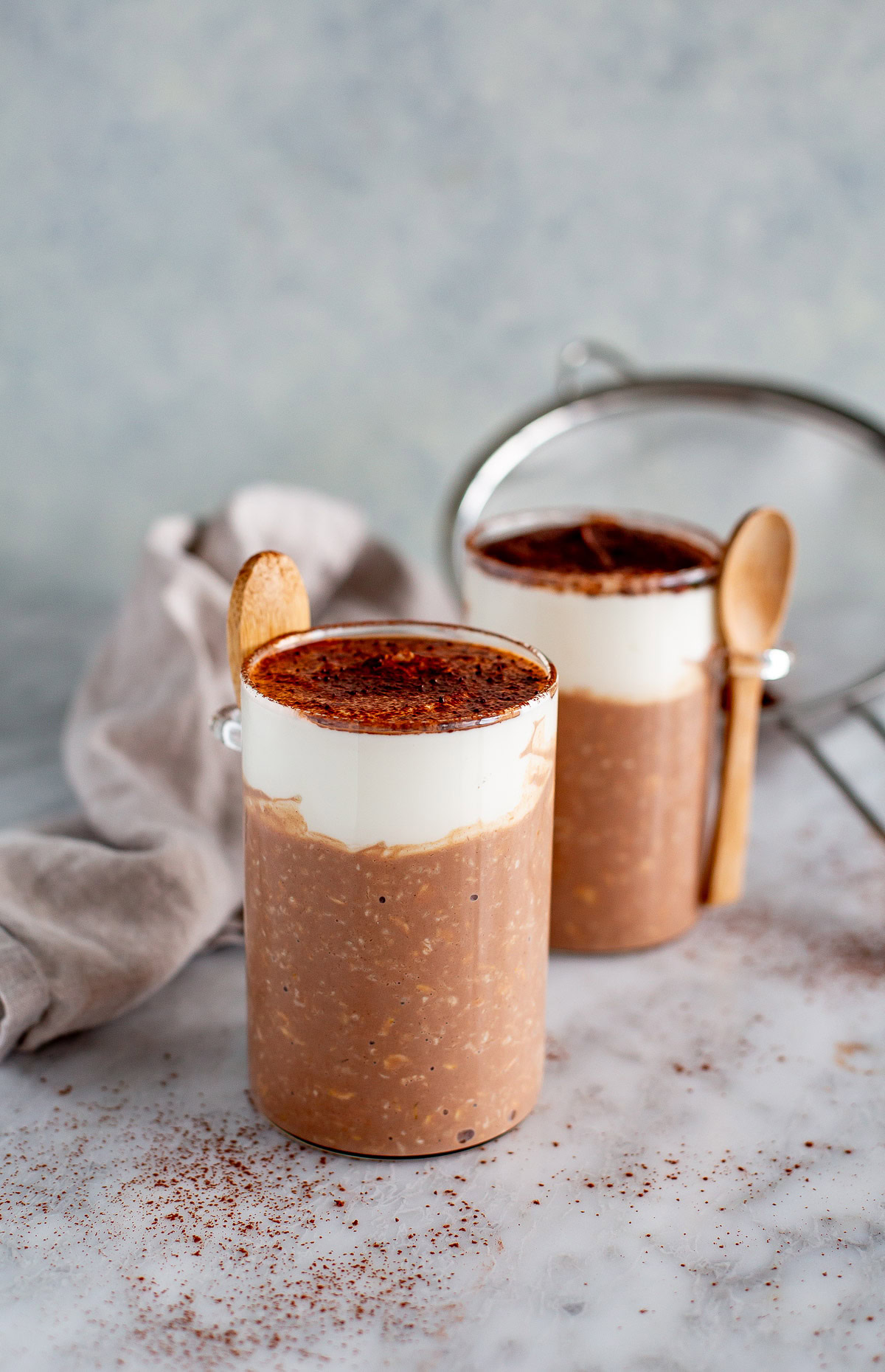 Side shot of two jars of Tiramisu Overnight Oats topped with a cream layer and dusted with cocoa powder.