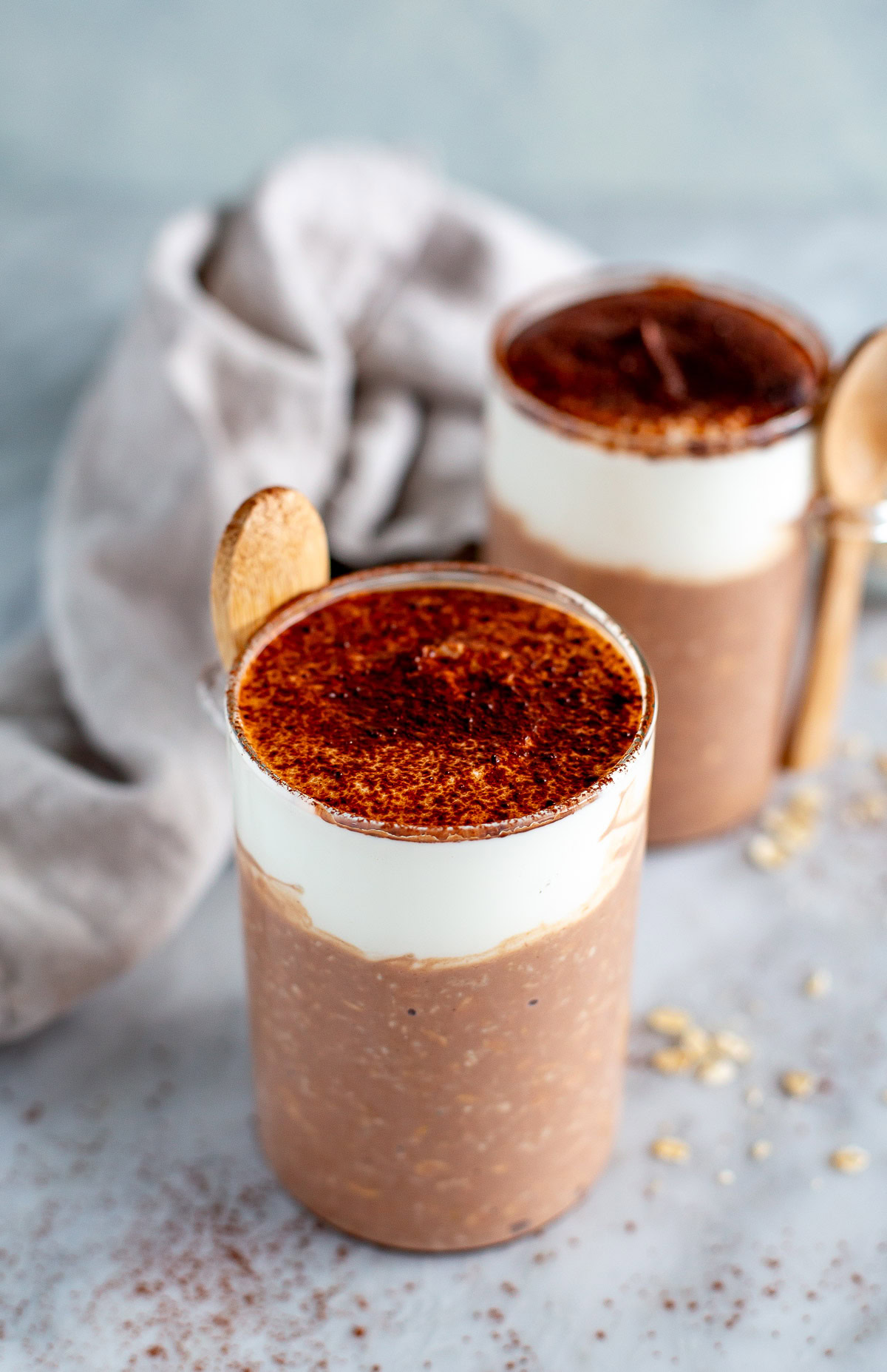 Side shot of two jars of Tiramisu Overnight Oats with a thick cream topping, dusted with cocoa powder.