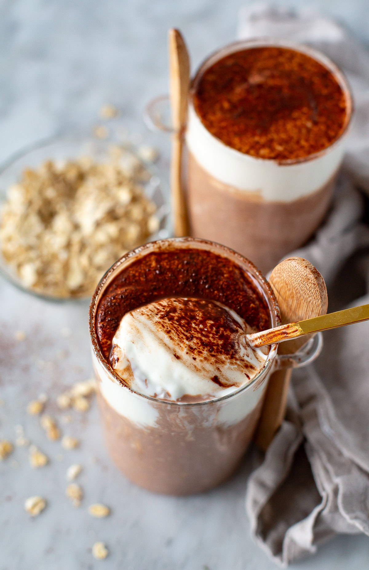 Overhead shot of two jars of Tiramisu Overnight Oats with a gold spoon scooping the creamy topping.