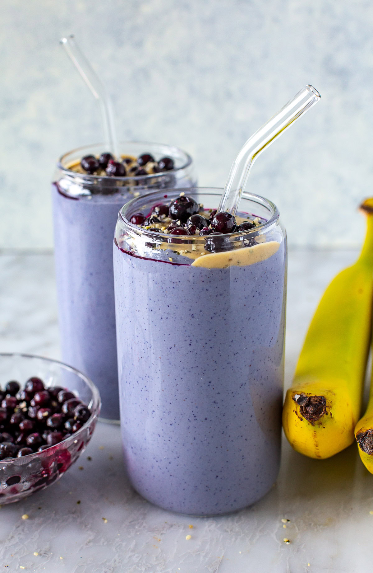 Side shot of two purple tofu smoothies topped with blueberries and peanut butter.