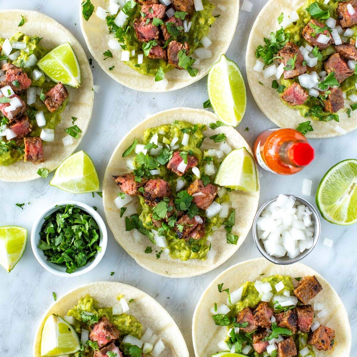 Assembled carne asada tacos garnishd with cilantro and lime wedges