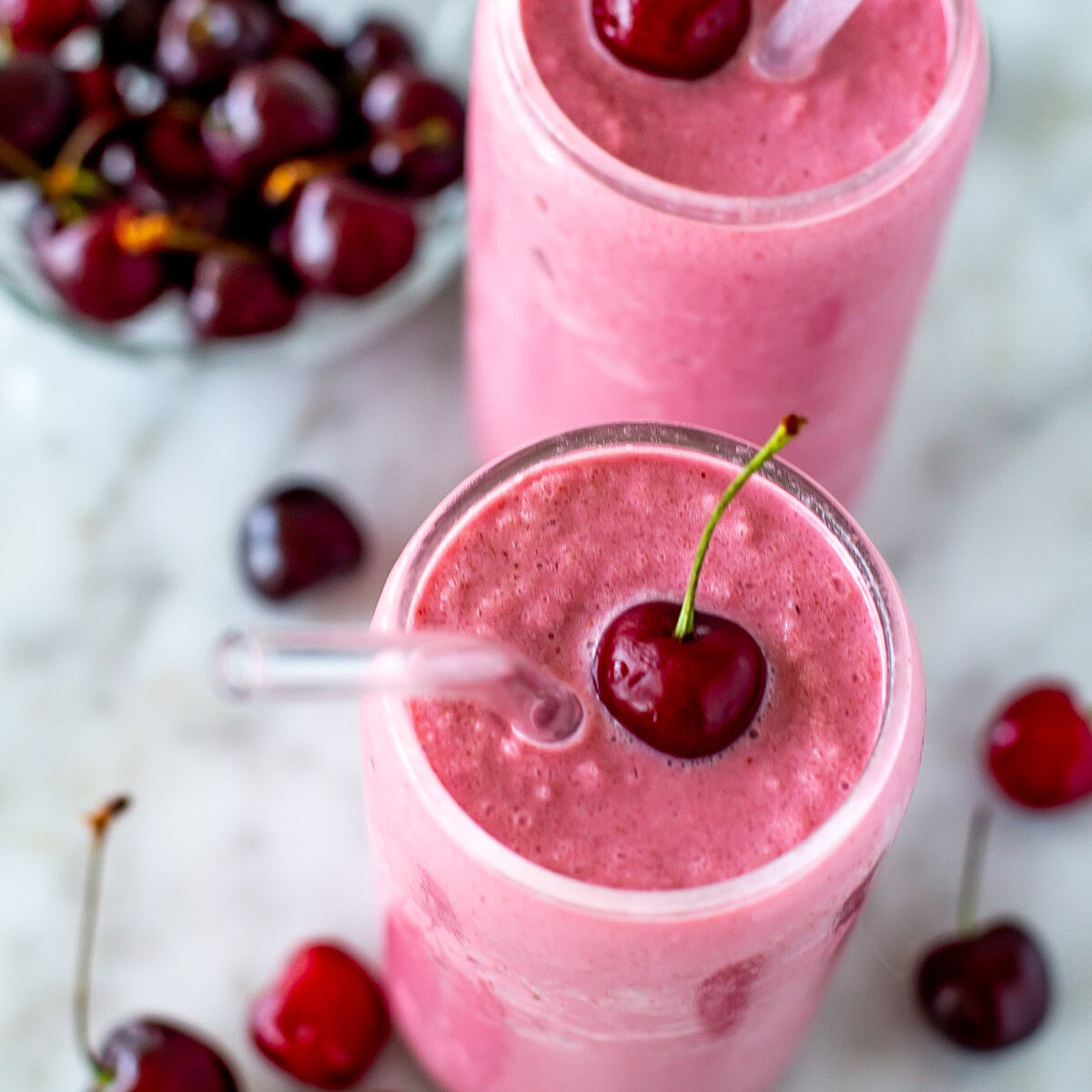 Overhead shot of two cherry smoothies with fresh cherries and straws.