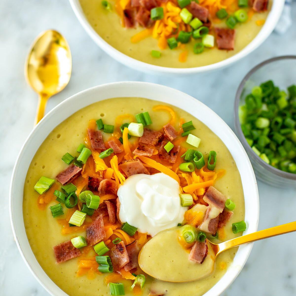 Two bowls of crockpot potato soup with a spoon in the bowl placed in the foregound.