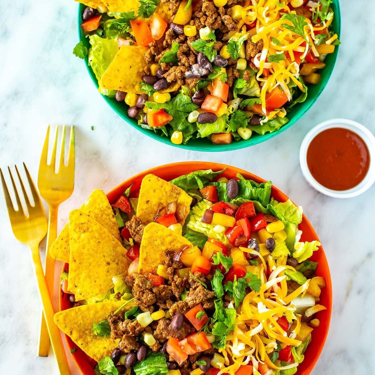 Two bowls of dorito taco salad with extra taco sauce on the side.
