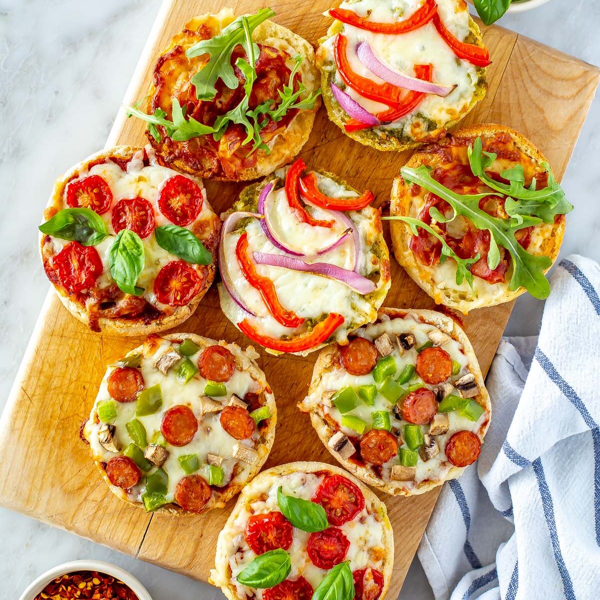 Several different English muffin pizzas on a butcher block.