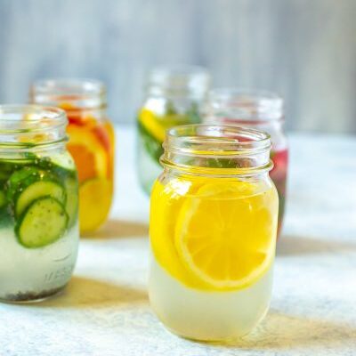 Lemon Water 5 Ways in mason jars. Focus on the lemon wedge water.
