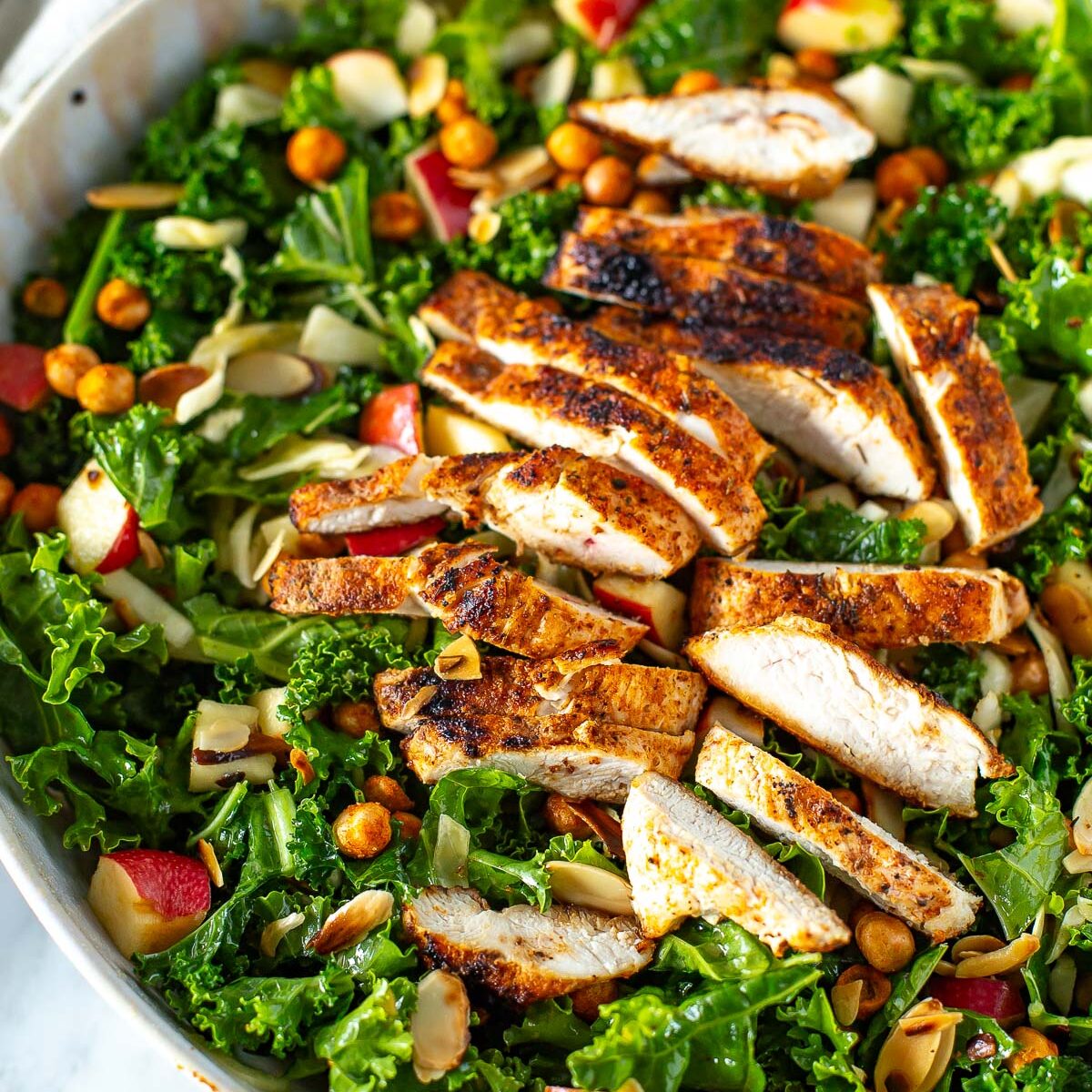 Overhead shot of a bowl of kale crunch salad with sliced chicken and dressing on the side.