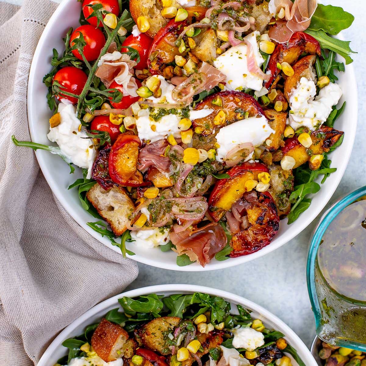 Overhead shot of two bowls of grilled peach burrata salad with various toppings.