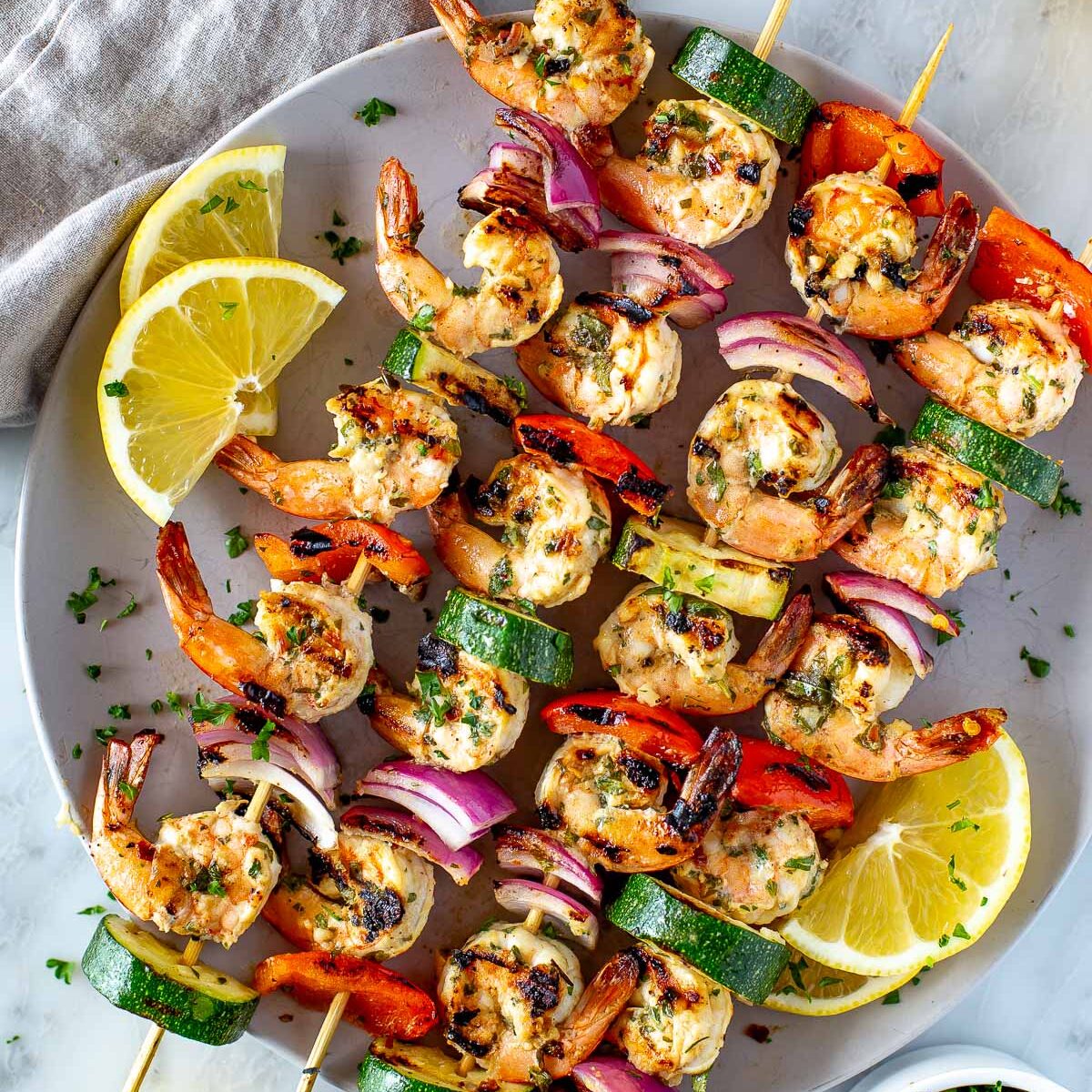 Overhead shot of cooked shrimp and vegetable skewers garnished with lemon and herbs on a serving platter 1