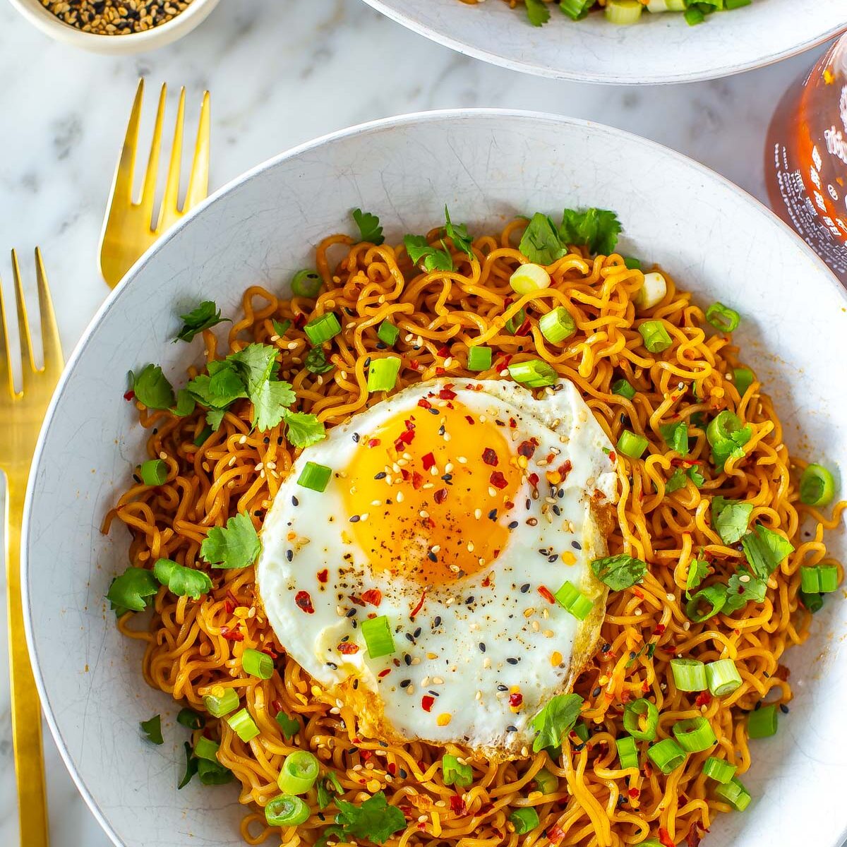 A close-up of a bowl of spicy noodles topped with a fried egg, green onions and cilantro.