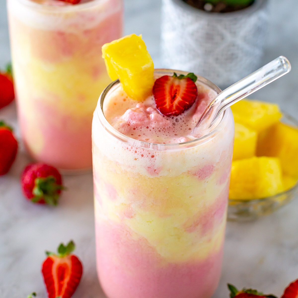 Side shot of a strawberry pineapple smoothie with a straw.