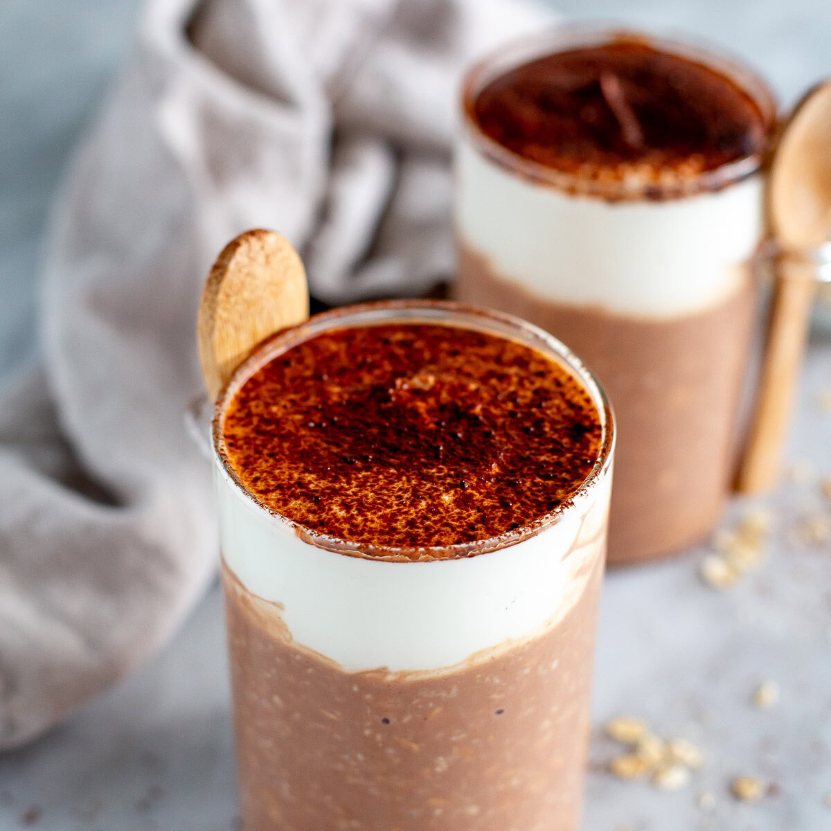 Side shot of two jars of Tiramisu Overnight Oats with a thick cream topping, dusted with cocoa powder.